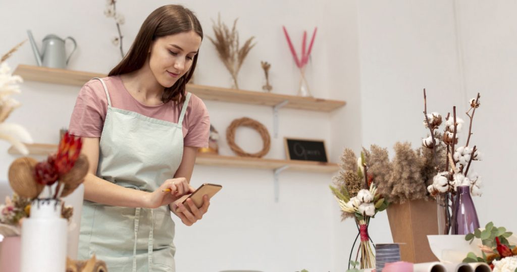 Mujer blanca de cabello largo, con un delantal en una floristería.